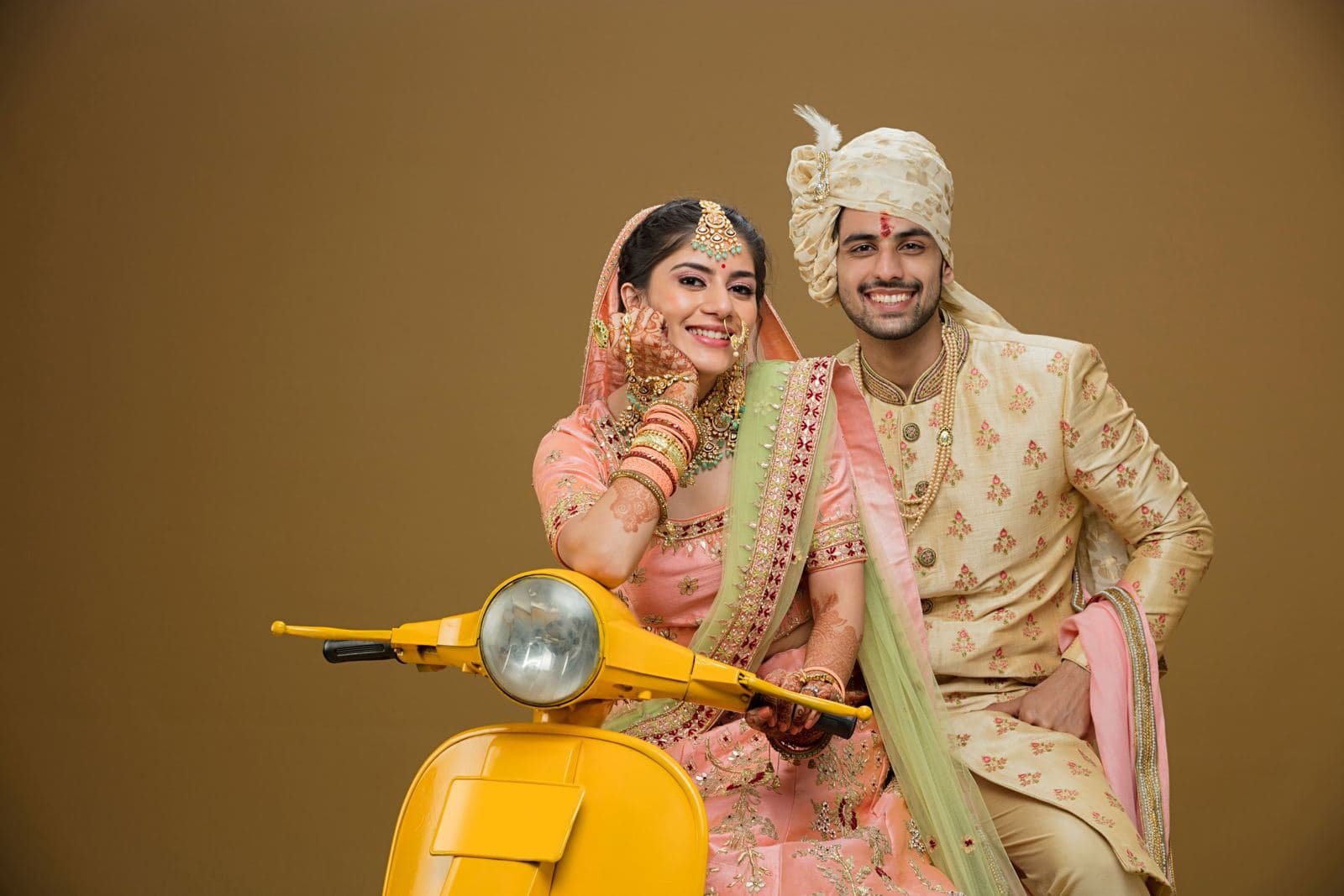 Couple in wedding wear posing playfully with a yellow scooter