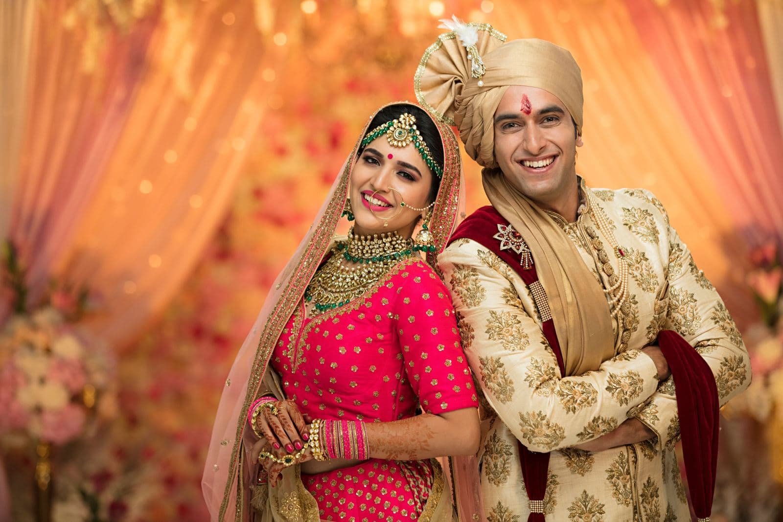 Couple in wedding attire posing before a floral backdrop