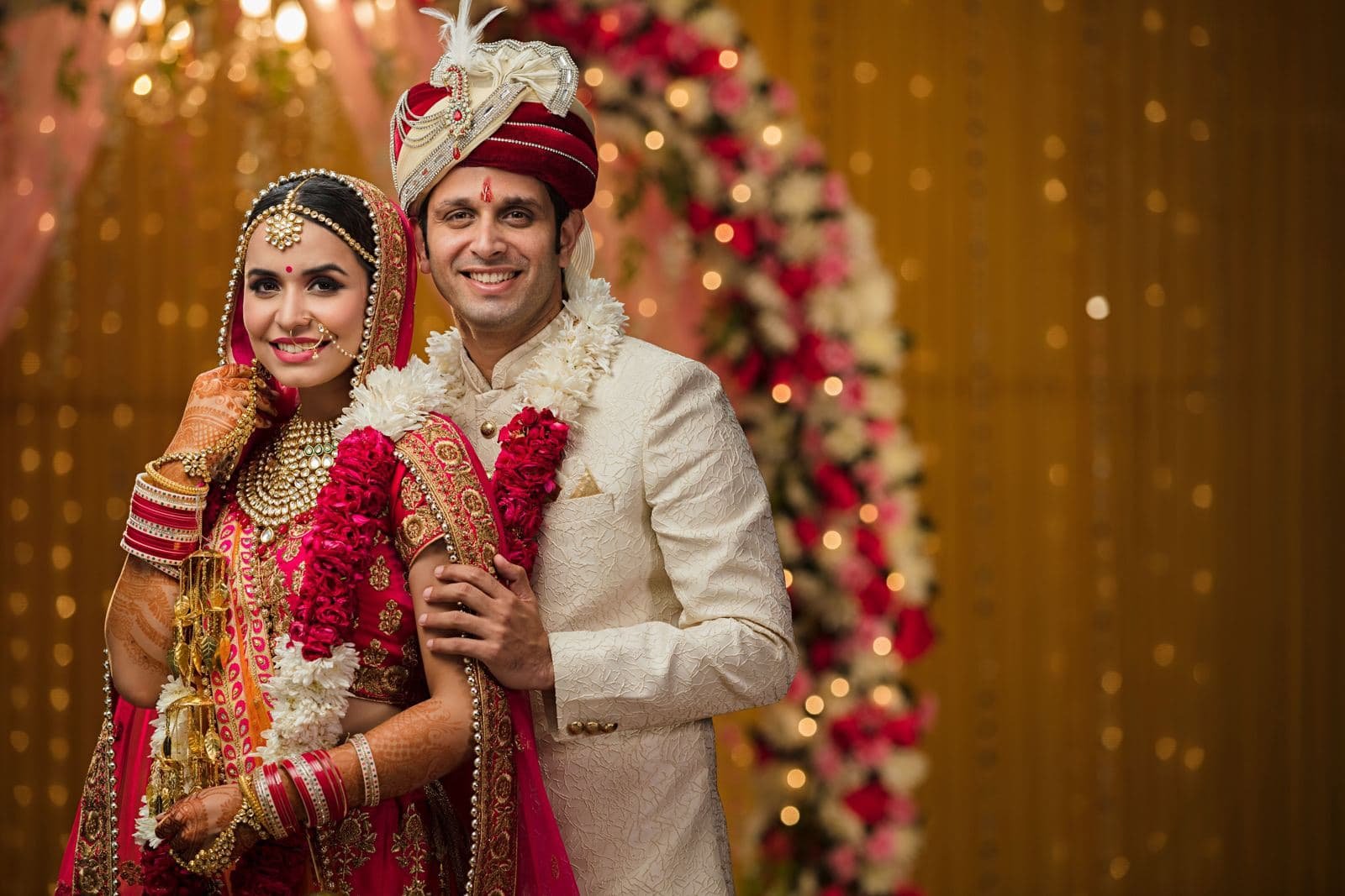 Groom and bride smiling under a floral mandap
